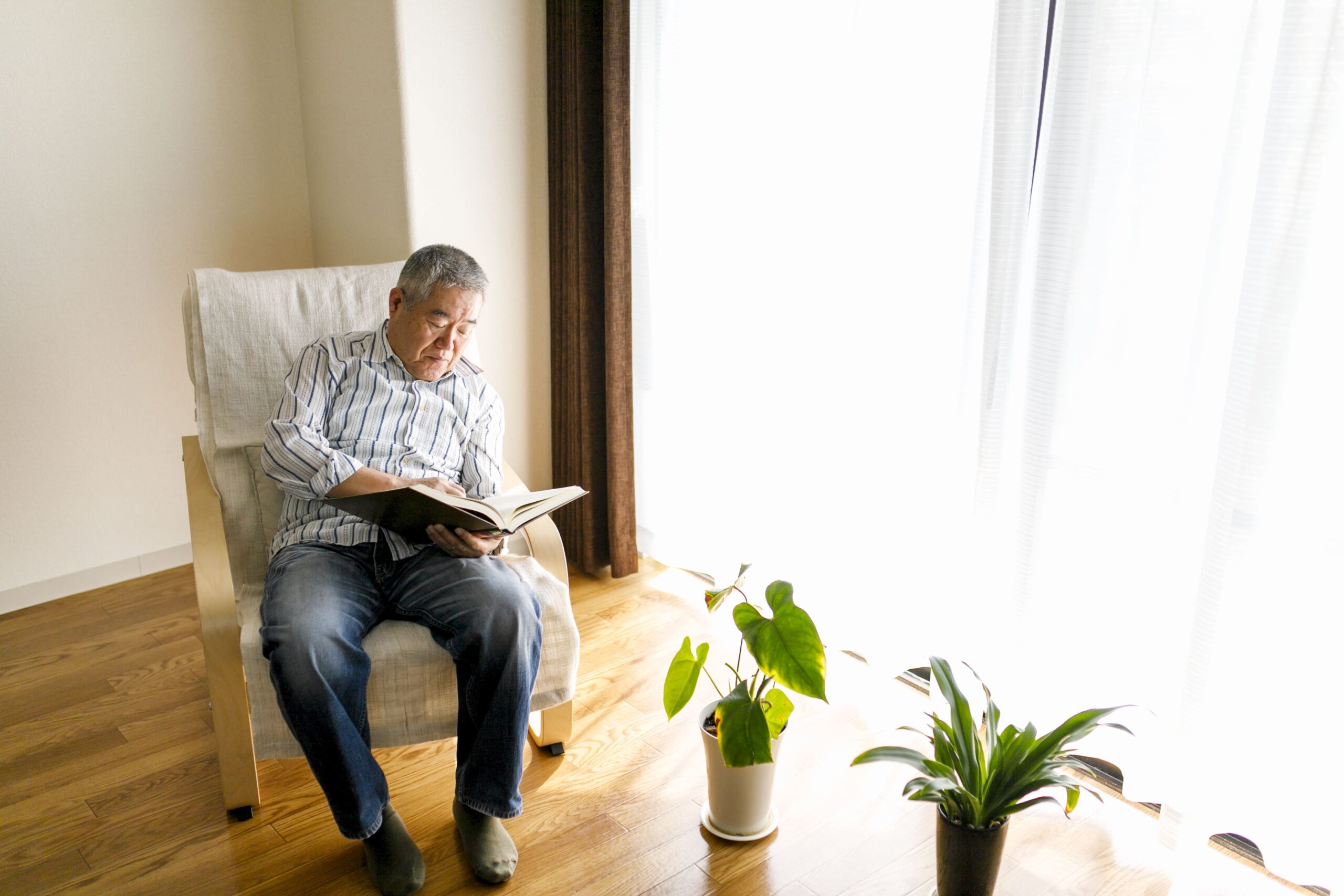 椅子に一人座って本を開く高齢の男性。葬儀後の“ふりかえり”を始める喪主・ご遺族の静かな時間