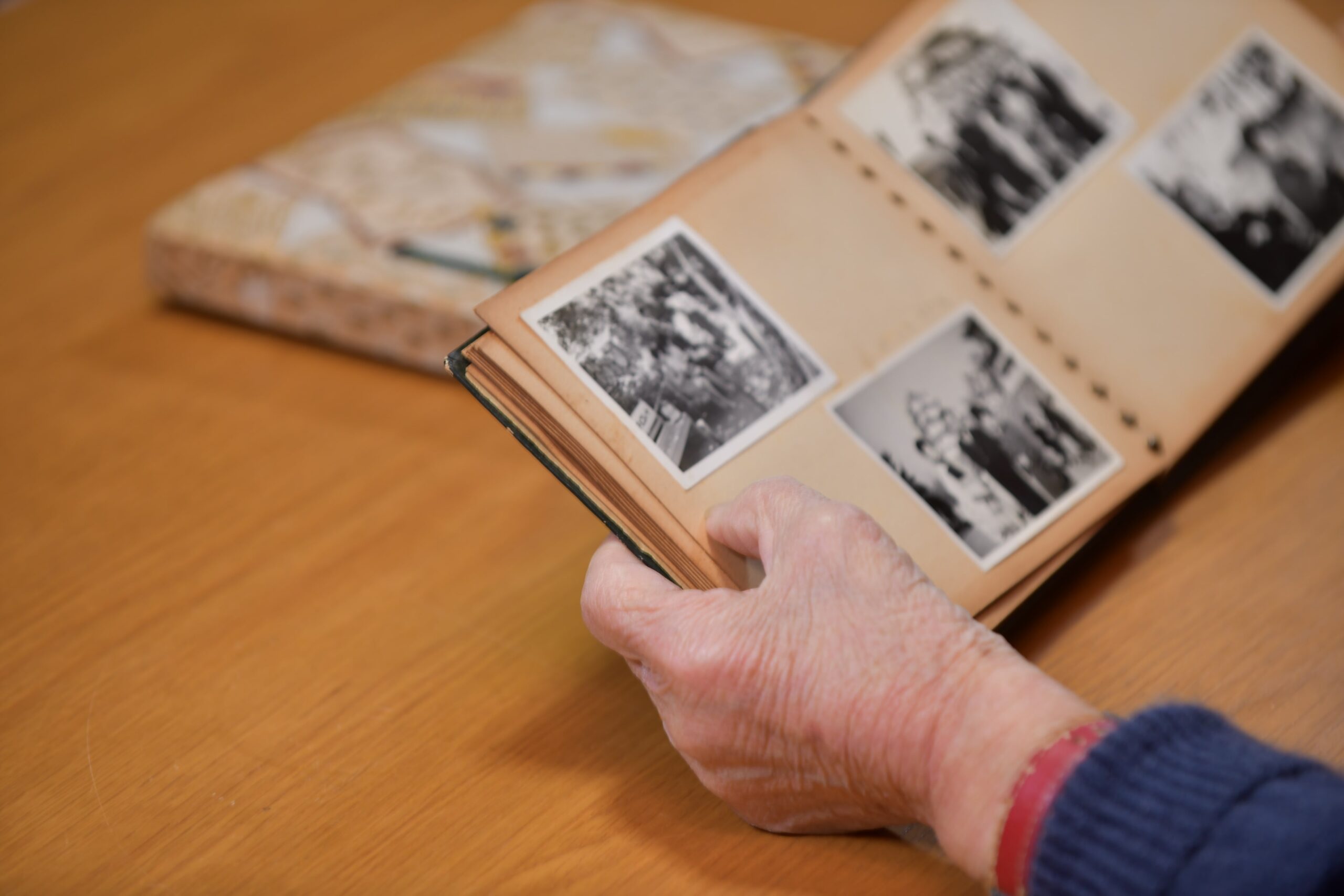 写真アルバムをめくる高齢者の手元。故人との思い出を語り、日常に「思い出を語る」時間を取り入れる場面