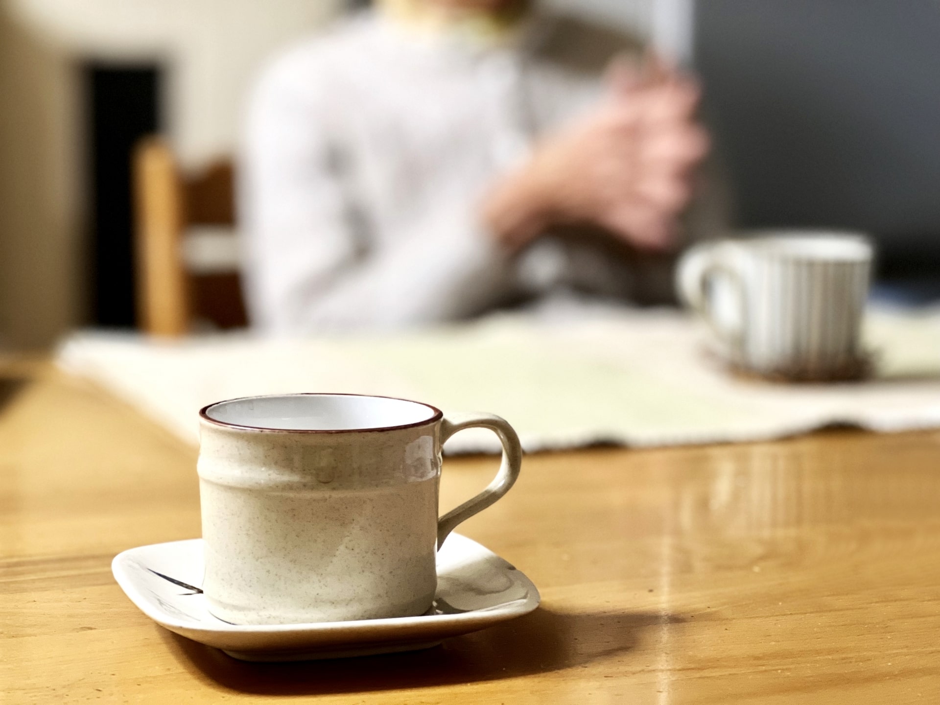 テーブルを囲みコーヒーを飲みながら語り合うご遺族や喪主。地域のサポート会、友人との気軽な会話を意図的に設けるイメージ画像。