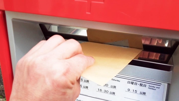 法事案内状の発送イメージ｜封筒をポストに投函する手元